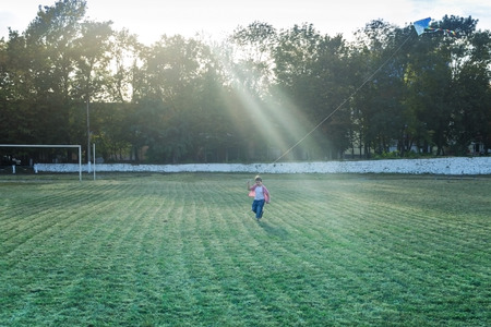 happy child girl with a kite running on meadow in summer in natureの写真素材