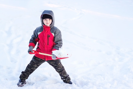 Portrait of a happy child in the winter who throws snow up a shovelの写真素材