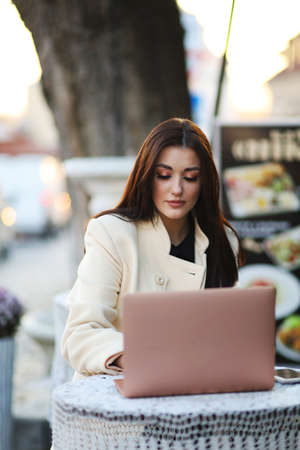 Self employed woman working with her phone and laptop in a restaurant terrace with a cup of coffee