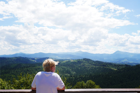 A man in bright clothes is resting on the grass in a high place in the Carpathians with a view of the mountains.の写真素材