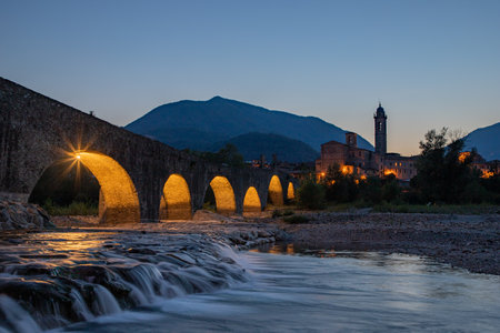 The Ponte Gobbo is an ancient bridge with an irregular profile, which crosses the Trebbia river in Bobbio in the province of Piacenza during sunset.の写真素材