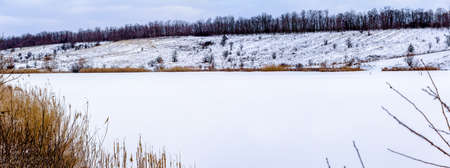 A frozen lake covered with white snow, trees grow along the banks. Ukraineの写真素材
