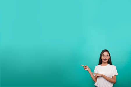 young asian indian woman wearing white t-shirt against sky blue background pointing finger right side of herself.の写真素材
