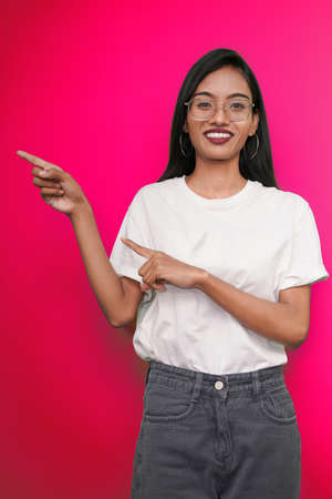young asian indian woman wearing white t-shirt against Pink background pointing finger right side of herself.の写真素材