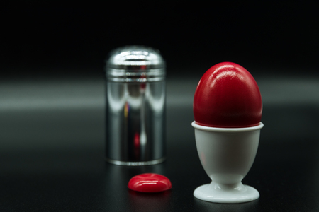 a red egg an an iron salt shaker and a white egg cupの写真素材