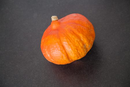 Close-up of little orange saturated ripe pumpkin in center of smooth black background surfaceの写真素材