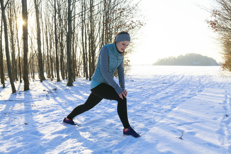 Female in winter is stretching after jogging in snow with trees in backgroundの写真素材