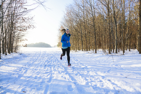 Femal in winter while jogging in snow with trees in backgroundの写真素材