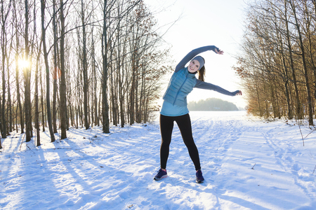 Femal in winter is stretching after jogging in snow with trees in backgroundの写真素材
