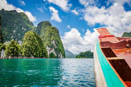 Wooden Thai traditional long-tail boat on a lake with mountains and rain forest in the background...