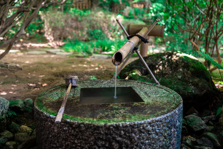 Ancient Zen stone wash basin with Japanese writings and water coming out of bamboo pipe in Ryoanji Temple, Kyoto, Japanの写真素材
