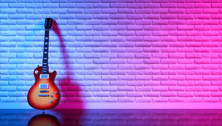 Electric guitar against a brick wall in neon light, 3d illustrationの写真素材