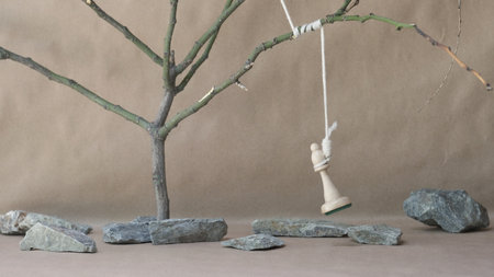 chess piece white bishop hanging on noose among stones on beige backgroundの写真素材