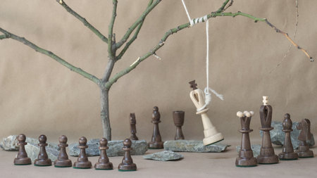 chess piece white king hanging on noose among black chess pieces on beige backgroundの写真素材