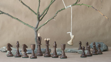 chess piece white pawn hanging on noose among black chess pieces on beige backgroundの写真素材