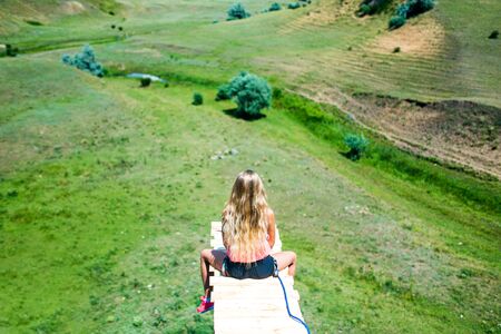 Woman sitting on a wooden ledge on a high mountain and view of the mountain landscape.