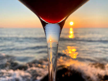 A glass of red wine on the background of the sea and sunsetの写真素材