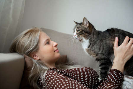 Young pretty woman with domestic cute cat is laying on sofa at homeの写真素材