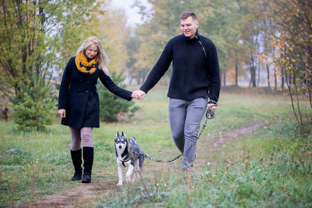 Young family couple with siberian husky dog walking in autumn parkの写真素材