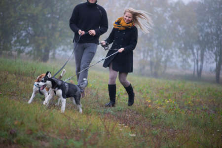 Happy young family couple with two dogs running in autumn parkの写真素材