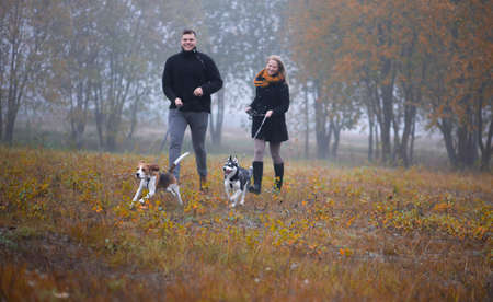 Happy young family couple with two dogs running in autumn parkの写真素材