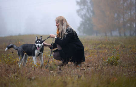 Young woman with beautiful siberian husky dog playing in city park during autumnの写真素材