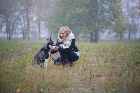 Young woman with beautiful siberian husky dog playing in city park during autumnの写真素材