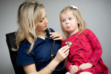 Friendly doctor female examining a little girl by stethoscopeの写真素材