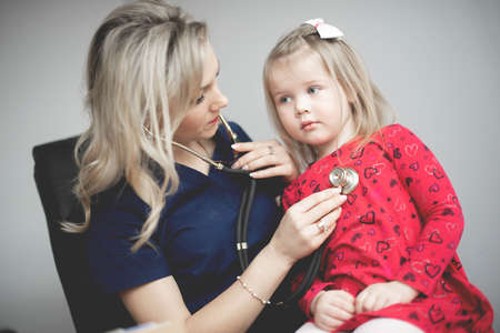 Friendly doctor female examining a little girl by stethoscopeの写真素材