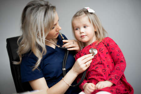 Friendly doctor female examining a little girl by stethoscopeの写真素材
