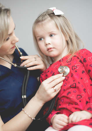 Friendly doctor female examining a little girl by stethoscopeの写真素材