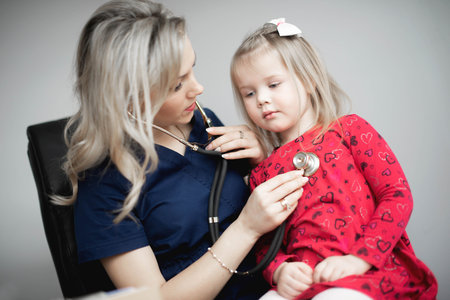 Friendly doctor female examining a little girl by stethoscopeの写真素材