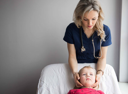 Friendly doctor female examining a little girl by stethoscopeの写真素材