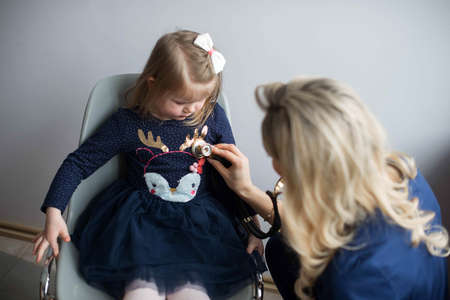Friendly doctor female examining a little girl by stethoscopeの写真素材