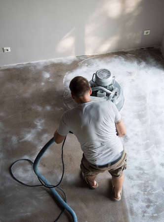 Construction worker in a family home living room that grind the concrete surface before applying epoxy flooring.Polyurethane and epoxy flooring.Concrete grinding.の写真素材