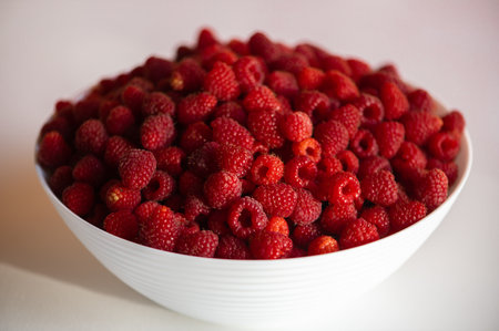 Fresh raspberries in a white bowl on the background of a green grass and autumn leavesの写真素材