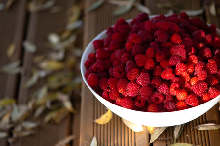 Fresh raspberries in a white bowl on the background of a green grass and autumn leaves