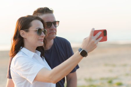Happy couple with age difference - a young woman and a middle aged man take a selfie on the beachの写真素材