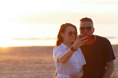 Happy couple with age difference - a young woman and a middle aged man take a selfie on the beachの写真素材