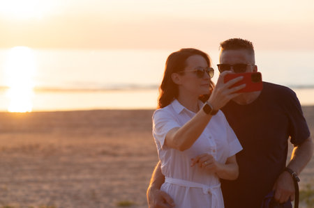 Happy couple with age difference - a young woman and a middle aged man take a selfie on the beachの写真素材