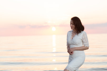 Young woman taking selfie through smart phone while standing at beach during sunsetの写真素材