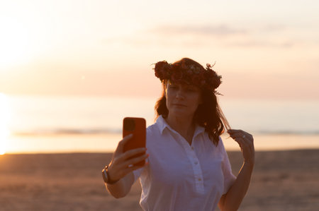 Young woman taking selfie through smart phone while standing at beach during sunsetの写真素材