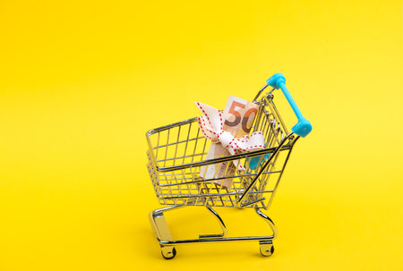 roll of euro banknotes with white ribbon in supermarket trolley cart isolated on yellow backgroundの写真素材