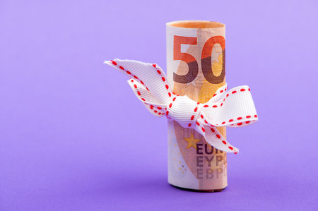 fifty euro banknote money roll tied with a white gift ribbon isolated on a purple backgroundの写真素材