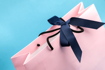 Pastel pink shopping or gift bag with dark ribbon on blueの写真素材
