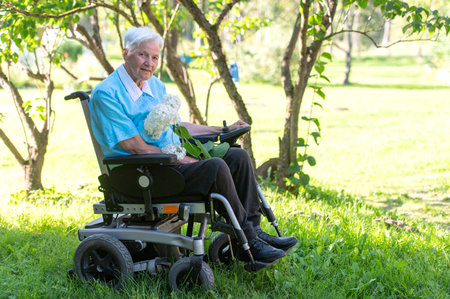 Sad senior woman in a wheelchair with a white hydrangea flowerの写真素材