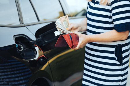 woman takes money dollars out of her wallet while standing next to a car with an open fuel tankの写真素材