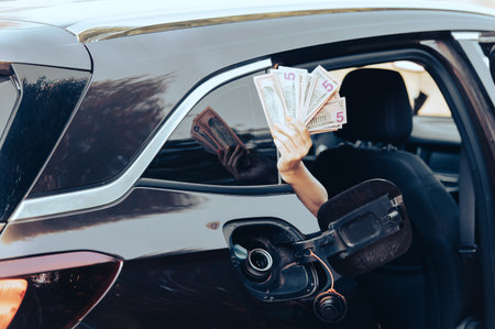 woman hand hold cash dollar bills next to car with an open tank, concept of rising fuel pricesの写真素材