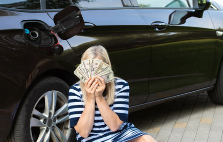 Desperate woman hides face behind cash near an open car fuel tank, concept of rising fuel pricesの写真素材