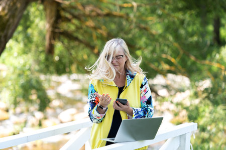 Attractive middle aged female using smartphone and laptop outdoorの写真素材